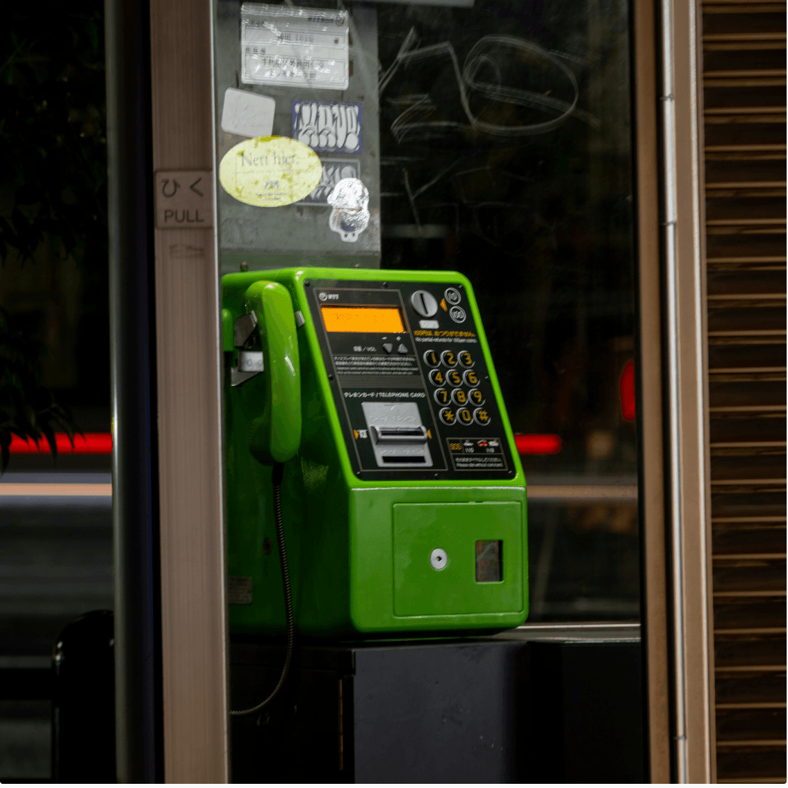Telefone público verde em uma cabine.